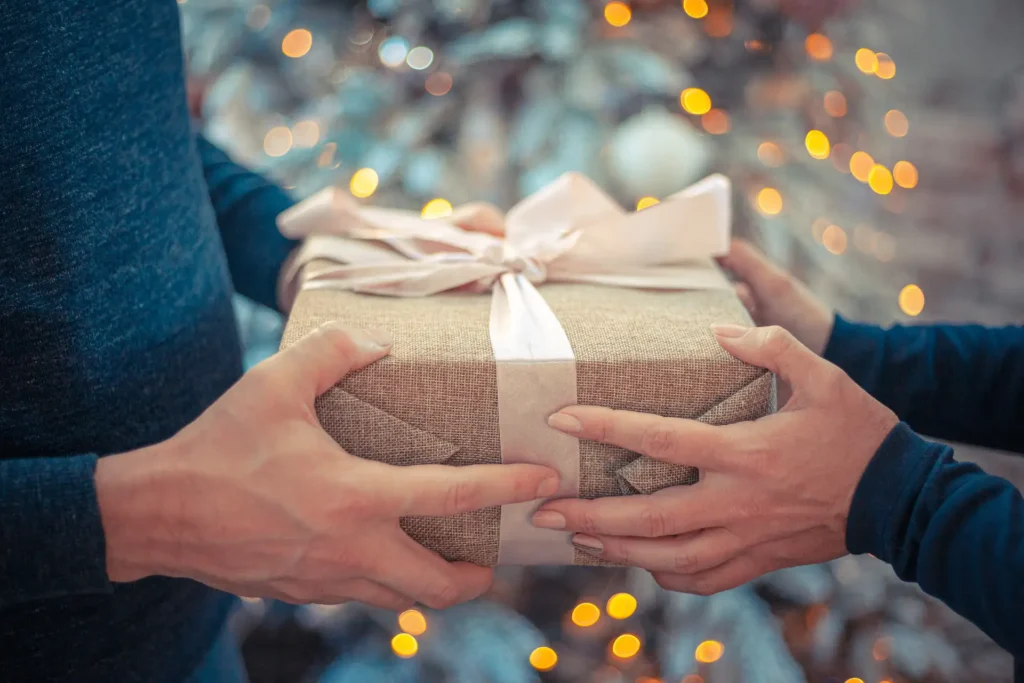 In the picture, a close-up of the hands of two people exchanging a gift.