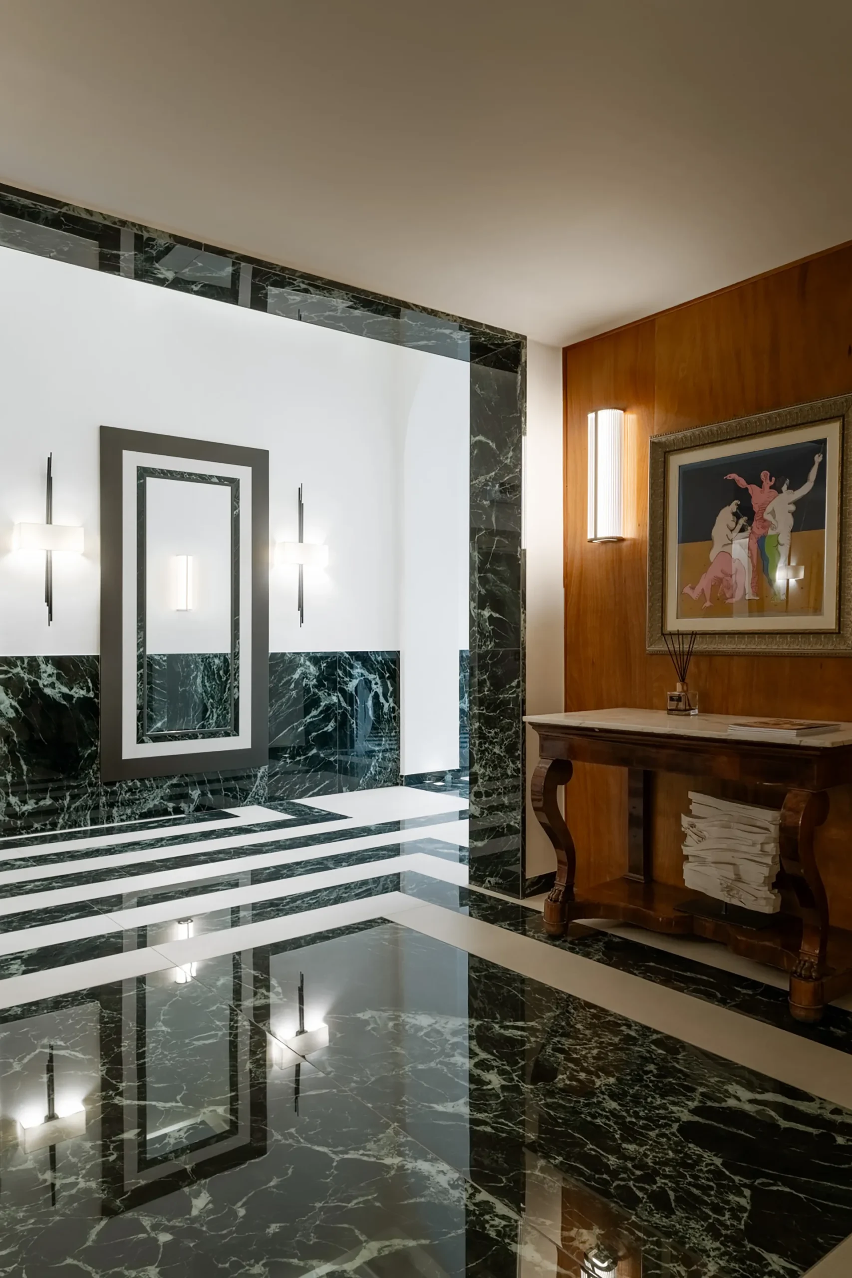 The image shows a common area at the Hotel Plaza: on the right, we can see a wooden table and a painting hanging on the wall. The floors are black and white marble.