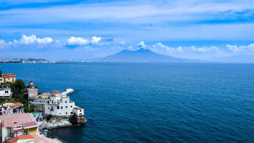 In the picture, a view of Naples with some houses on the left and the sea with the Vesuvius in the background.