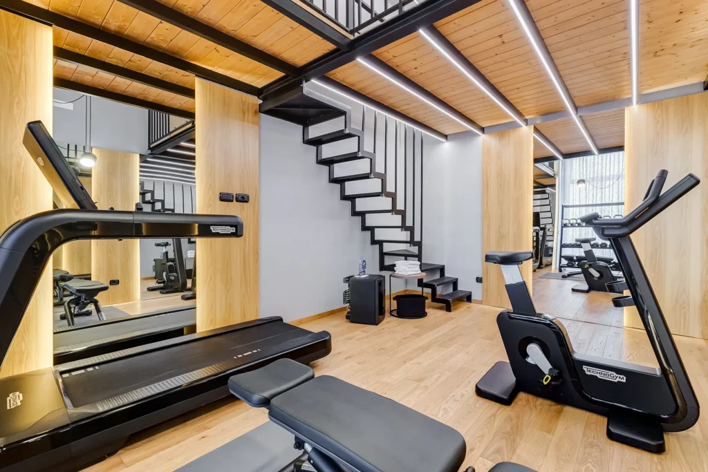 The picture shows the Gym of the Hotel Plaza: on the left, we can see a treadmill, while on the right, there is an exercise bike. Mirrors surround the gym and, at the back, a staircase leads to the upper floor.