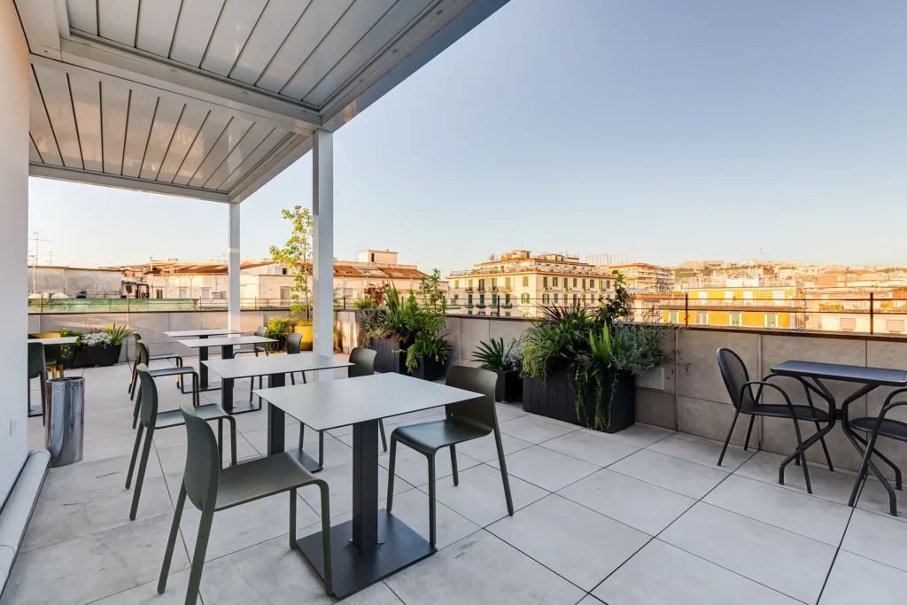 In the picture, the terrace of the Hotel Plaza with tables and chairs. Potted plants are scattered around.